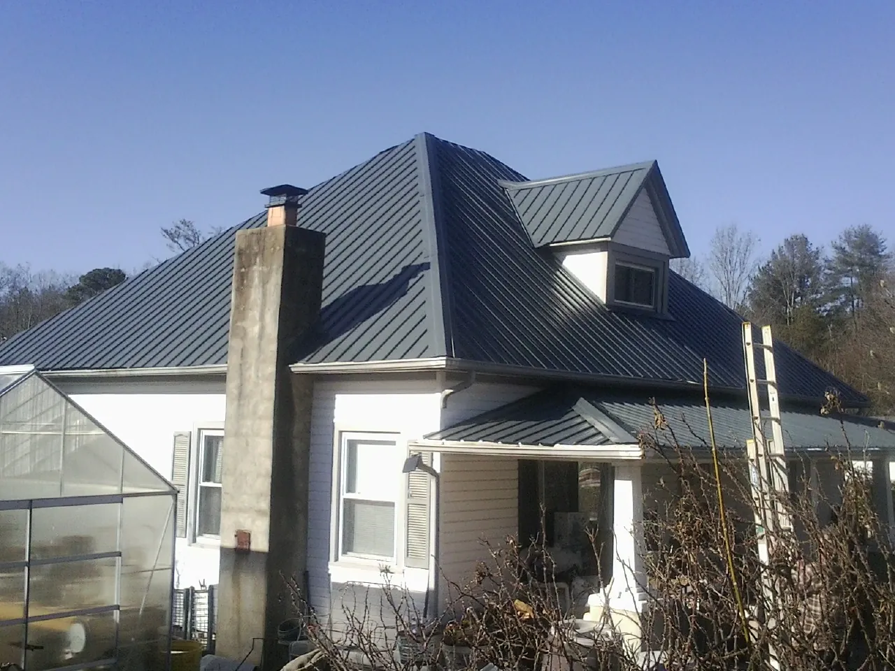 Dark blue standing seam metal roof on a white farmhouse with dormer — Slate & Tile Roof Repair by Roofing Brothers in Saddle River