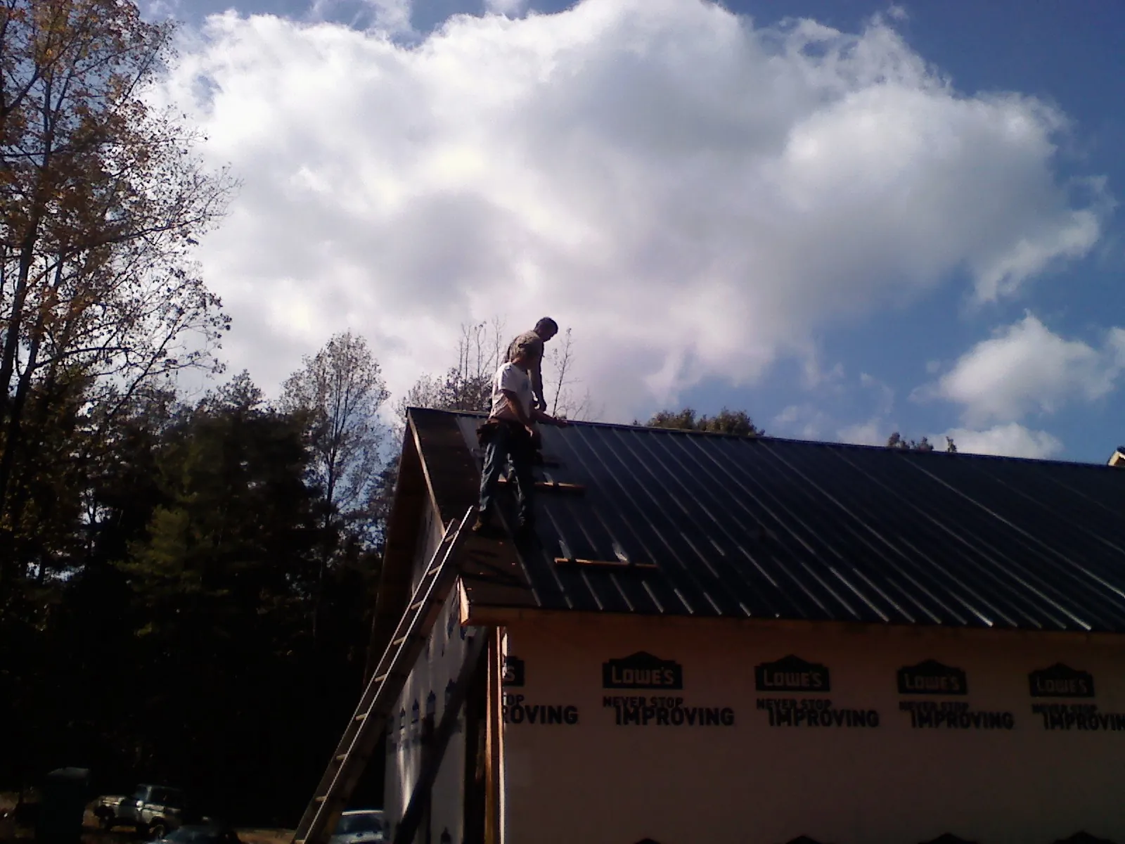 Roofer fastening dark metal panels high against a cloudy sky, from a Roof Inspection job in Saddle River
