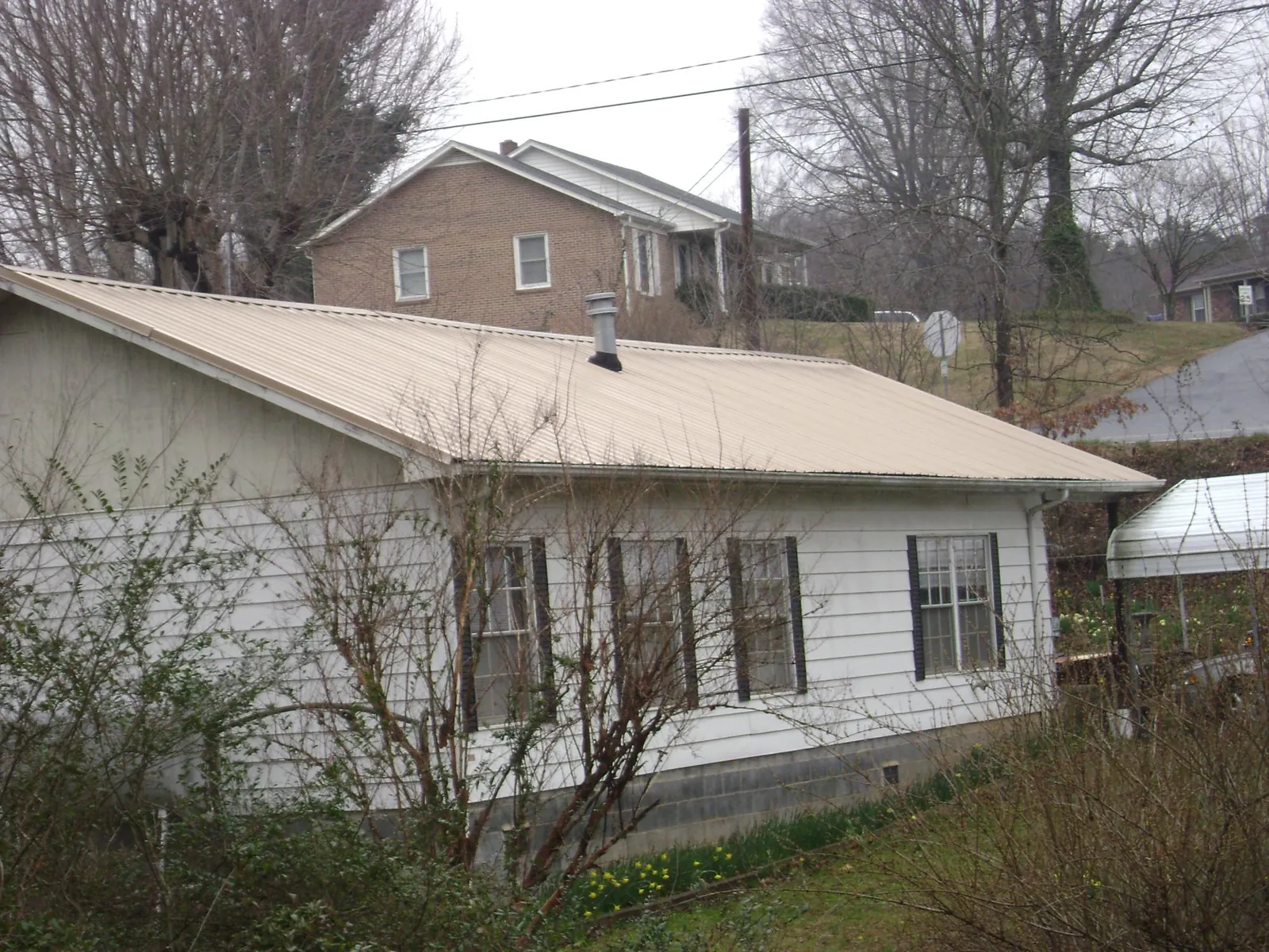 Tan metal roof on a white sided house set into a hillside — Commercial Roofing by Roofing Brothers in Saddle River